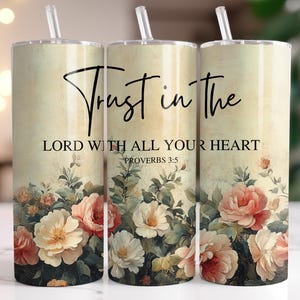 May include: Three cylindrical tumblers with clear straws, featuring a cream-colored background with a floral pattern of pink, white, and green flowers. The text reads Trust in the LORD WITH ALL YOUR HEART PROVERBS 3:5 in black lettering.