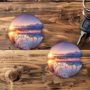 May include: Two car coasters with a sunset design, featuring text that reads "Looking for that blessed hope...Jesus Christ." The coasters have a semi-circular shape with a notch for easy removal. The background is a wooden surface.