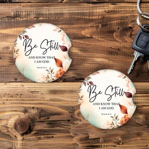 May include: Two car coasters with floral designs and the text "Be Still and Know That I Am God, Psalm 46:10." The coasters have a white background with a floral border in shades of peach, brown, and green.