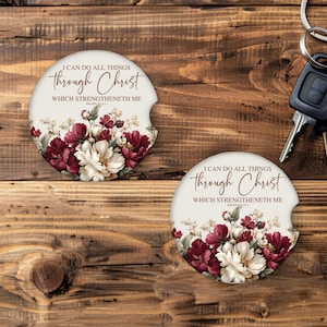 May include: Two off-white car coasters with floral designs and the text "I CAN DO ALL THINGS through Christ WHICH STRENGTHENETH ME." The coasters feature burgundy and white flowers. Keys are in the background.