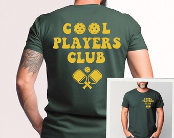 May include: A dark green t-shirt with the text "COOL PLAYERS CLUB" in yellow with a yellow pickleball and paddle design.