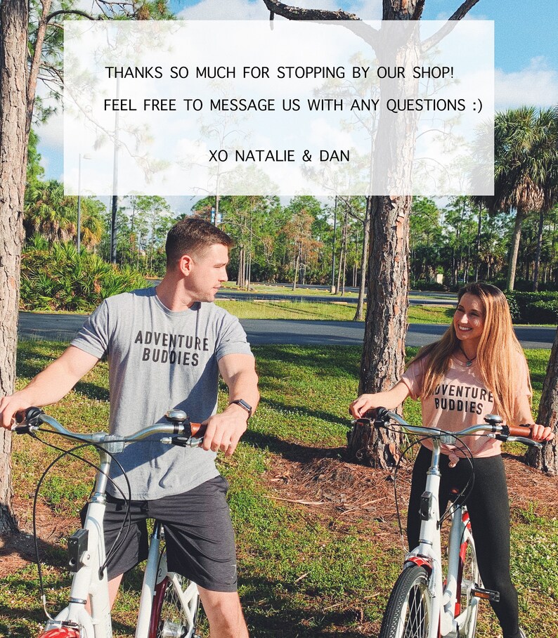 Op de afbeelding: Twee mensen fietsen op een pad in een park. Ze dragen allebei T-shirts met de tekst "Adventure Buddies". De tekst "THANKS SO MUCH FOR STOPPING BY OUR SHOP! FEEL FREE TO MESSAGE US WITH ANY QUESTIONS :) XO NATALIE & DAN" wordt weergegeven op een witte achtergrond.
