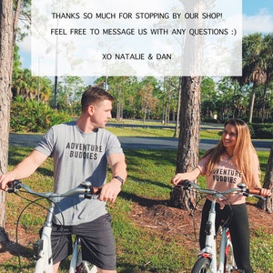 Op de afbeelding: Twee mensen fietsen op een pad in een park. Ze dragen allebei T-shirts met de tekst "Adventure Buddies". De tekst "THANKS SO MUCH FOR STOPPING BY OUR SHOP! FEEL FREE TO MESSAGE US WITH ANY QUESTIONS :) XO NATALIE & DAN" wordt weergegeven op een witte achtergrond.