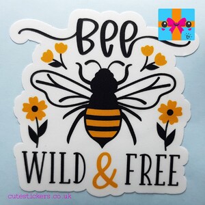 May include: A white sticker featuring a black and yellow bee illustration with the words "BEE WILD & FREE" in black and orange. The design includes yellow flowers. The website address cutestickers.co.uk is at the bottom.