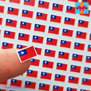 May include: A sheet of small, red, white and blue Taiwanese flag stickers. The stickers are arranged in a grid pattern. A finger is holding one of the stickers.