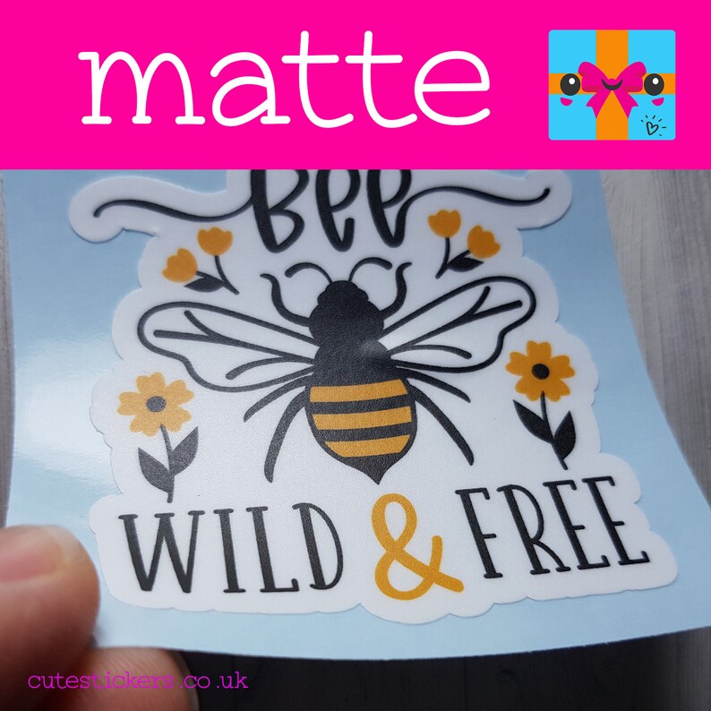 May include: A matte sticker featuring a bee illustration with the words "BEE WILD & FREE" in black and yellow. The bee has black and yellow stripes, with yellow flowers and leaves. The sticker is on a light blue background.