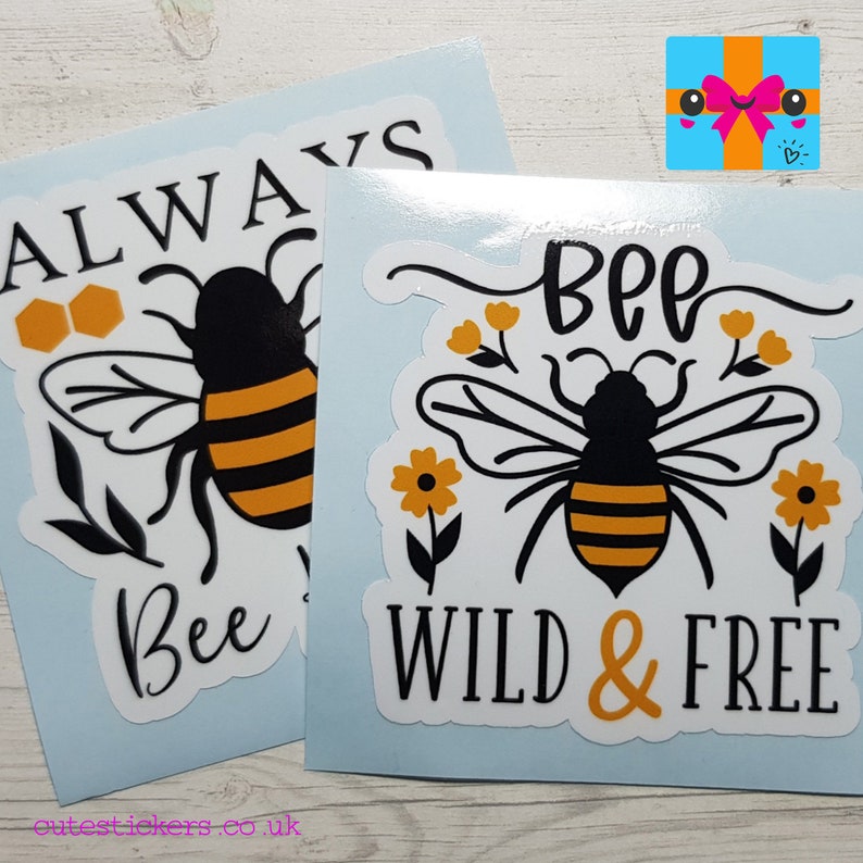 May include: Two stickers with bee-themed designs. One says "ALWAYS Bee" with a bee and honeycomb graphic. The other says "BEE WILD & FREE" with a bee and floral accents. Both stickers feature black, yellow, and white colors.