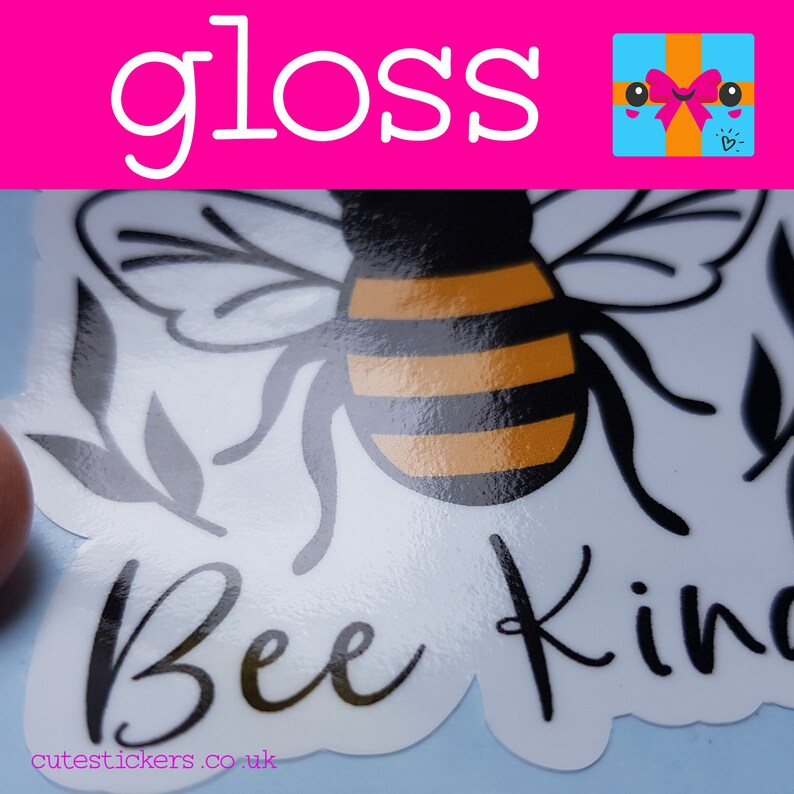 May include: Glossy sticker featuring a black and yellow bee with the words "Bee Kind" in a cursive font. The sticker has a white background and a pink banner at the top with the word "gloss" in white.