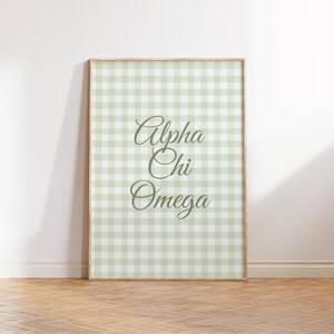 May include: A framed print with the Greek letters Alpha, Chi, and Omega in a decorative script. The background is a light green and white gingham pattern. The frame is a light wood colour.