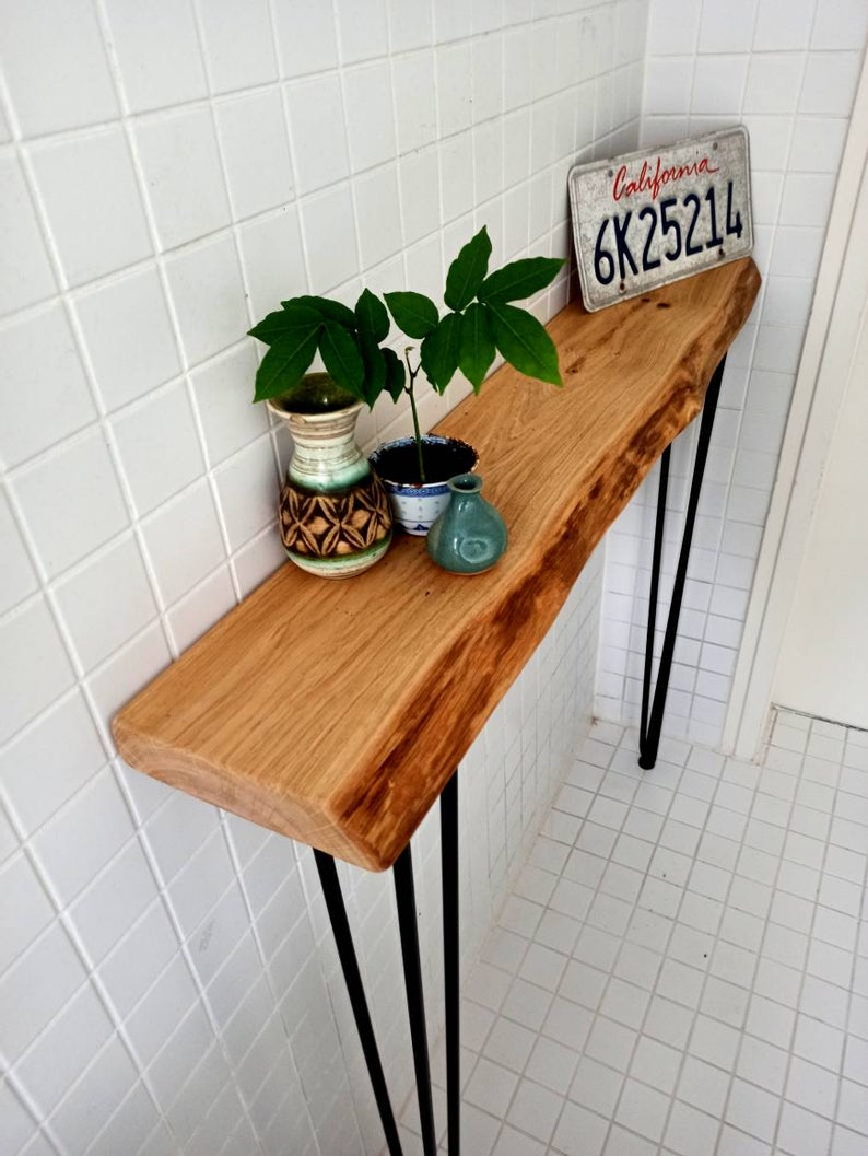May include: A wooden console table with a live edge top and black hairpin legs. The table is decorated with a small potted plant, a ceramic vase, and a California license plate that reads "6K25214".