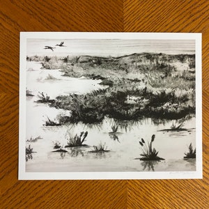 May include: A black and white print of a landscape with a marsh and two birds flying overhead.