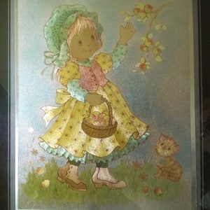 May include: A framed illustration of a young girl in a yellow dress and bonnet reaching for apples on a tree branch. She carries a basket of apples, with a small cat nearby. The artwork has a vintage, storybook style.