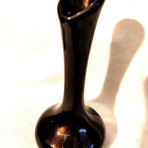 May include: A black ceramic vase with a flared opening and a rounded base. The vase has a glossy finish.