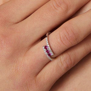 Peut inclure: Une bague en argent avec un design incurvé présente une rangée de petites pierres précieuses rouges et une rangée de petites pierres précieuses blanches.
