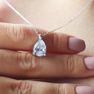 May include: A silver chain necklace with a teardrop-shaped pendant featuring a large, clear, sparkling gemstone.