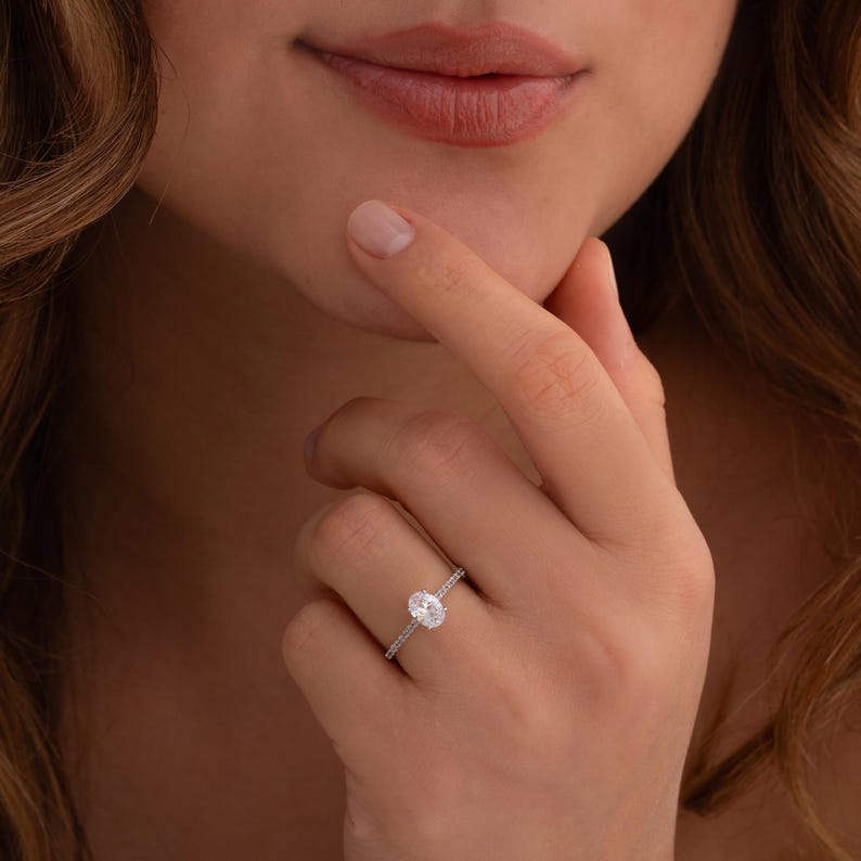 May include: A silver ring with an oval-shaped center stone and smaller stones set in a pave setting around the center stone.