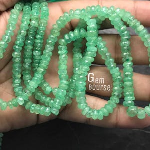 May include: A strand of emerald green gemstone beads. The beads are faceted and have a slightly irregular shape. The beads are strung on a clear thread and are approximately 3 mm in diameter.