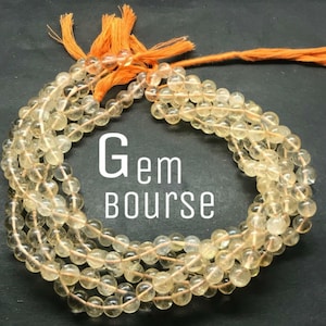 Puede incluir: Un collar de cuentas redondas translúcidas de color amarillo pálido dispuestas en un patrón circular, asegurado con borlas de color naranja brillante en la parte superior. El texto Gem bourse está impreso en blanco sobre el fondo oscuro.