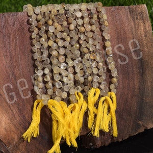 Puede incluir: Hebras de cuentas facetadas de piedras preciosas de color amarillo claro con borlas amarillas. Las cuentas son pequeñas y redondas, ensartadas para crear un collar o pulsera. Las borlas son de hilo amarillo.
