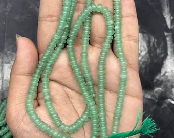 May include: A long strand of small, round, translucent light green beads strung on a thin green thread. The beads have a smooth, polished finish and are uniform in size and shape, creating a continuous line of soft green color across the palm.