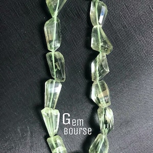 May include: A strand of faceted, translucent light green gemstone beads strung on a thin green cord. The beads have an irregular, elongated shape with multiple flat surfaces. The text Gem bourse is printed in white in the center of the image.
