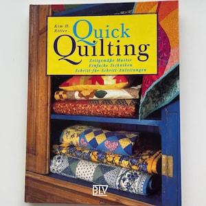 Könnte beinhalten: Ein Buch mit dem Titel "Quick Quilting" mit einem gelben Banner und blauen Buchstaben. Das Buchcover zeigt eine farbenfrohe Darstellung von Quilts und Kissen. Das Buch ist von Kim H. Ritter und enthält Text auf Deutsch.