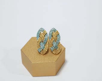 May include: A pair of gold and blue knotted earrings. The earrings are oval shaped and have a woven design.