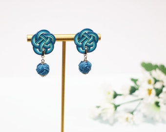 May include: A pair of blue and green earrings with a knotted design. The earrings are hanging from a gold stand.