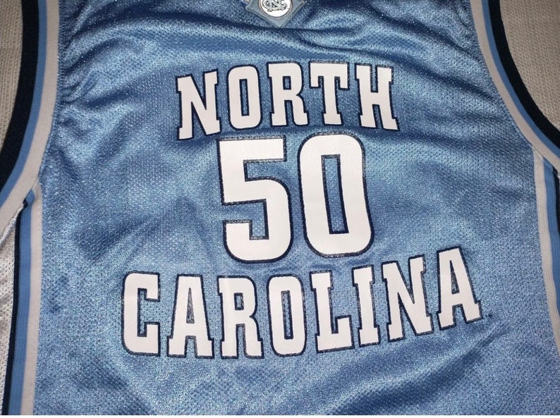 May include: A light blue basketball jersey with white lettering that reads "NORTH CAROLINA" and the number "50".