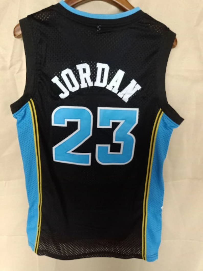 May include: Black basketball jersey with blue and yellow trim. The back of the jersey has the name "JORDAN" and the number "23" in white.