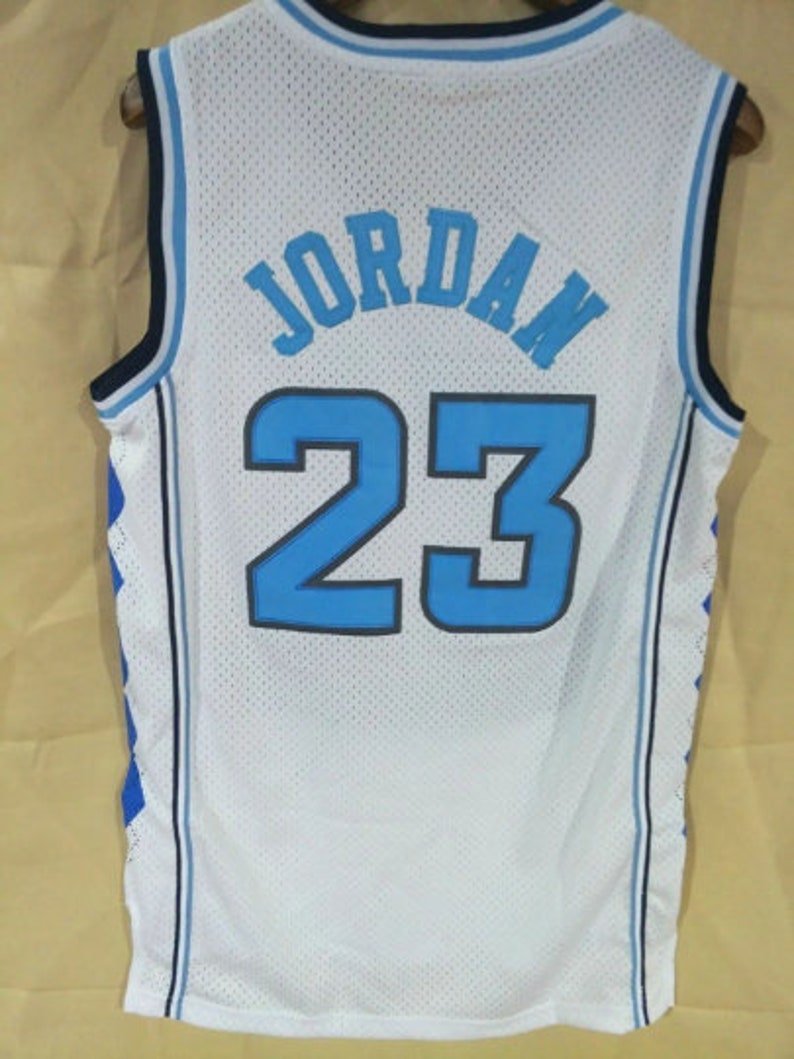 May include: White basketball jersey with blue and black trim. The back of the jersey has the name "JORDAN" and the number "23" in blue.