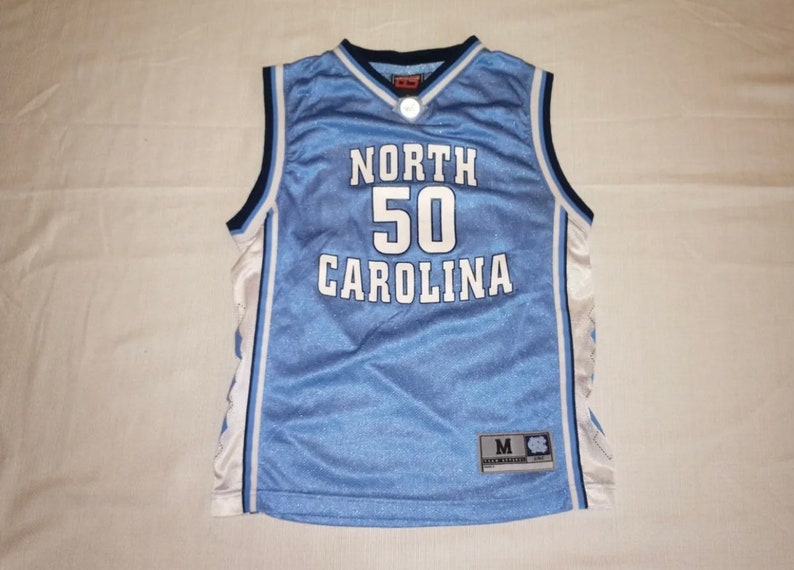 May include: A light blue basketball jersey with white and navy blue trim. The jersey has "NORTH 50 CAROLINA" printed on the front in white. The jersey has a size tag that says "M".