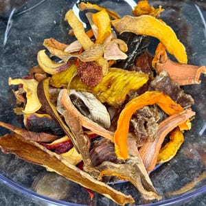 May include: A clear bowl filled with dried fruit, seen in close-up. The fruit pieces are a mix of colours, including yellow, orange, brown, and red. The assortment includes slices and pieces of various shapes and sizes.