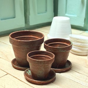 May include: Miniature terracotta plant pots and saucers are grouped with white, ribbed, cone-shaped items. The pots are different sizes and sit on a light wooden surface, hinting at a gardening or craft project.