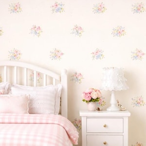 Puede incluir: Una escena de dormitorio en miniatura con una cama blanca, una mesita de noche y una alfombra. La cama tiene un edredón y almohadas de cuadros rosas. Las paredes son de color crema con detalles florales. Una lámpara y flores están en la mesita de noche.
