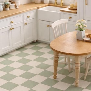 May include: Miniature kitchen scene with white cabinets, a wooden countertop, and a light green and white checkered floor. A small wooden table with two white chairs is set in the center. The kitchen is decorated with small plants and accessories.