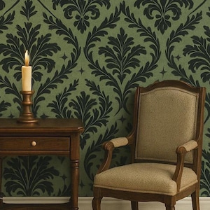 May include: A candle burns atop a wooden candlestick on a small, dark wooden side table. The table has a single drawer. A beige upholstered chair with wooden arms sits to the right. The background is a green wallpaper with a black floral pattern.