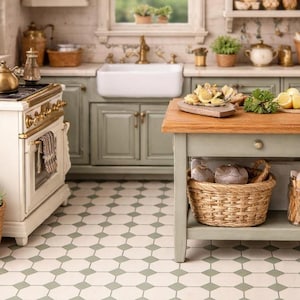 May include: A miniature kitchen scene with a white and gold stove, sage green cabinets, and a wooden island. The island holds a basket of bread and a wooden tray with lemons. A small potted plant sits on the floor.
