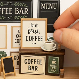 May include: Miniature coffee bar scene with signs that read "Coffee Bar", "Menu", and "But first, coffee". Includes a small coffee cup, a tiny chalkboard, and framed botanical prints. A hand is placing a miniature item.