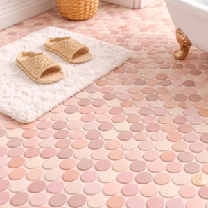 May include: A bathroom scene featuring a white clawfoot tub with gold-colored feet, a fluffy white bath mat, and woven sandals. The floor is covered in a mosaic of pink and peach-colored penny tiles, creating a soft, inviting atmosphere.