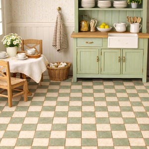 Può includere: Una scena di cucina in miniatura con un tavolino apparecchiato per il tè, un mobile verde e un pavimento a scacchi. Il tavolo è apparecchiato con tazze, piattini e un piccolo vaso di fiori. Un cestino e un canovaccio appeso completano l'atmosfera.