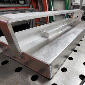 May include: A silver metal toolbox with a carrying handle. The toolbox is empty and has a smooth, brushed finish.