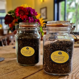 May include: Two glass jars filled with loose leaf tea. The jars have yellow labels with black text that reads "Darjeeling 2nd Flush SFTGFOP" and "Darjeeling 1st Flush SFTGFOP".