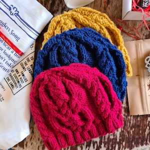 May include: Three knitted hats stacked on top of each other. The top hat is yellow, the middle hat is blue, and the bottom hat is red.