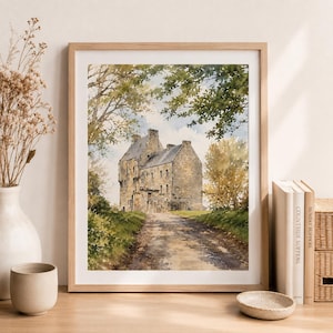 May include: A framed watercolor painting depicting a stone castle situated at the end of a dirt path, surrounded by green trees and foliage under a light sky. The artwork is presented in a light wood frame, capturing a landscape scene.