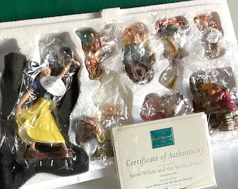 May include: A Snow White and the Seven Dwarfs ornament set, displayed in a green box with a white foam insert. The set includes figurines of Snow White and the dwarfs, with a certificate of authenticity.