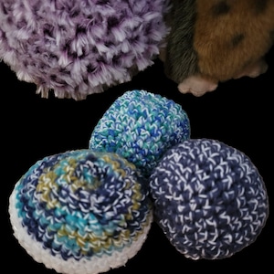 May include: A selection of handmade crochet balls in various colours. The balls are in shades of blue, green, white, and purple. The textures vary from fluffy to tightly woven. These could be used as toys or decorative items.
