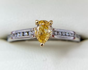 May include: A pear-shaped yellow diamond engagement ring with a white gold band and smaller diamonds set in the band.