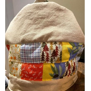 Può includere: Un copriteiera in tessuto beige con un design a patchwork. Il patchwork include motivi floreali, a quadri e ad albero in tonalità di rosso, giallo, blu e verde.