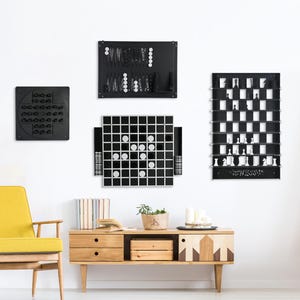 Op de afbeelding: Een set van vier zwarte, ingelijste magnetische spelborden, waaronder een schaakbord, een damspelbord, een vier-op-een-rij-bord en een negen-op-een-rij-bord. De borden hangen aan een witte muur boven een houten consoletafel.